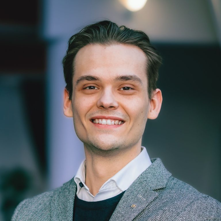 Jesse Luhtala hymyilee, harmaa bleiseri ja valkoinen kauluspaita