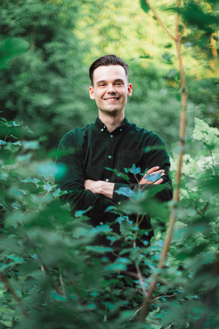 Jesse Luhtala seisoo kädet ristissä vihreän kasvillisuuden keskellä